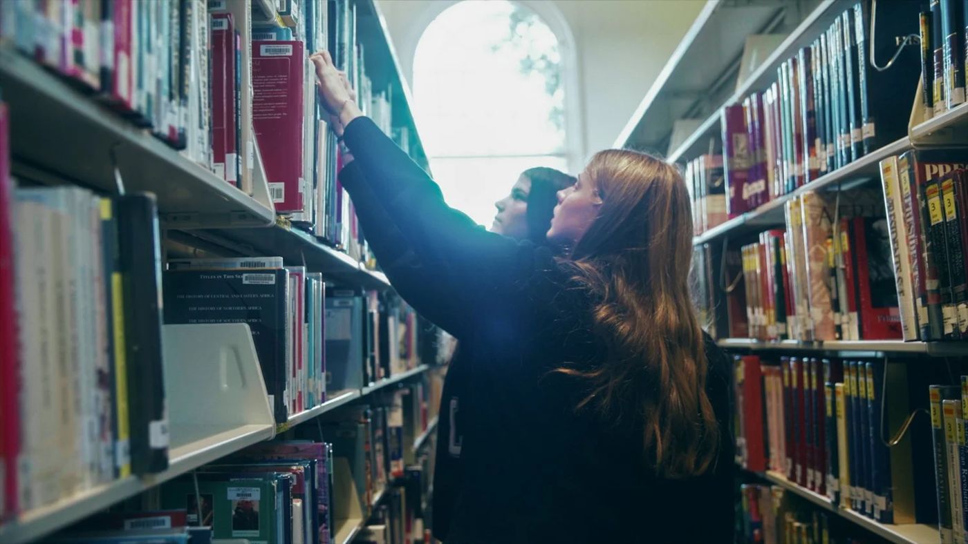 A student filmed among the library stacks during a Creative Intensive shoot